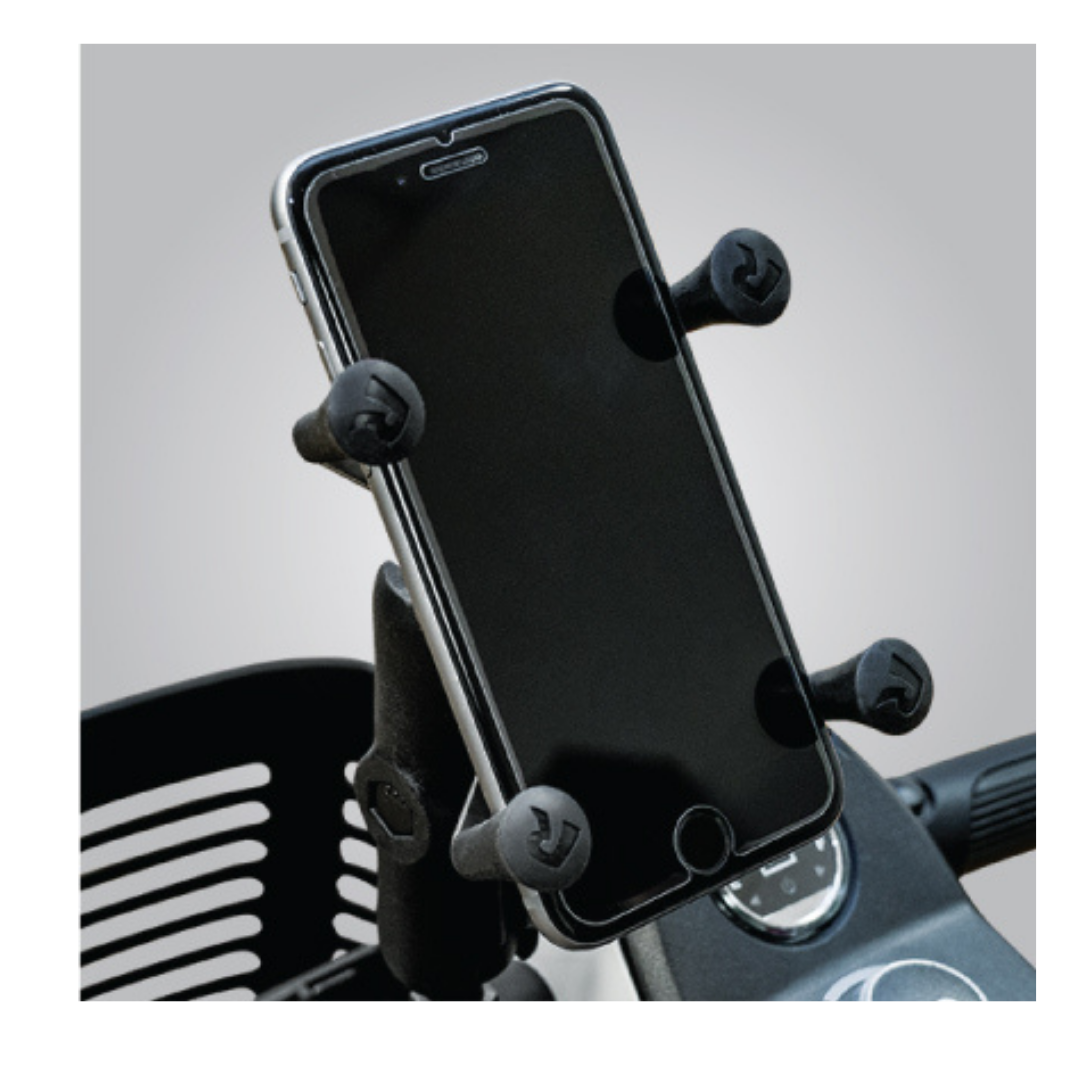 A Pride Mobility RAM® X-Grip® Cell Phone Holder secures a smartphone upright on a scooter or motorcycle, with part of the dashboard and a wire basket in the background.